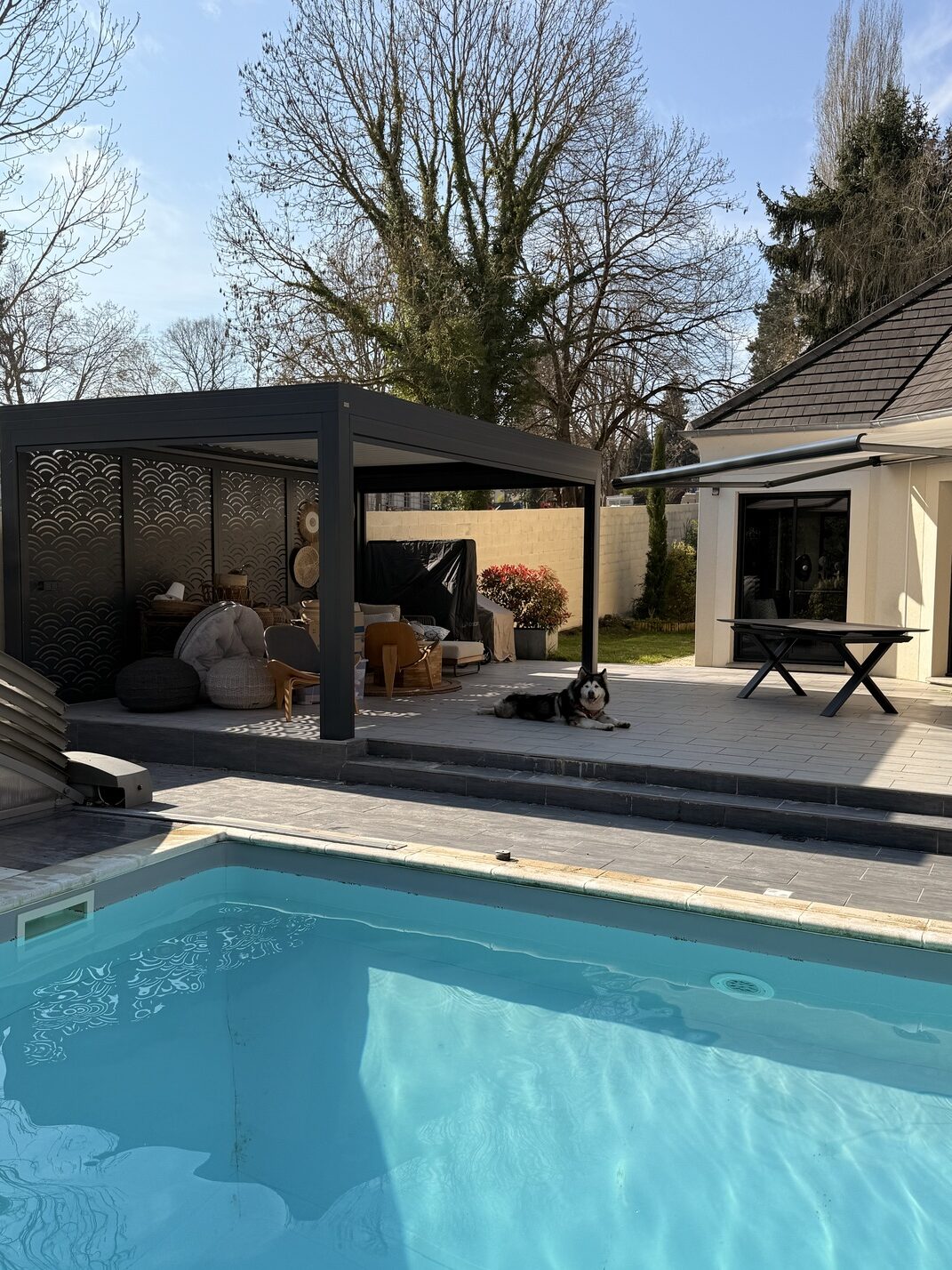 Pergola bioclimatique et store banne installés sur la même maison, terrasse et piscine